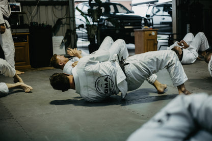 Men doing BJJ drills on grey mats wearing while BJJ gis branded with GMA