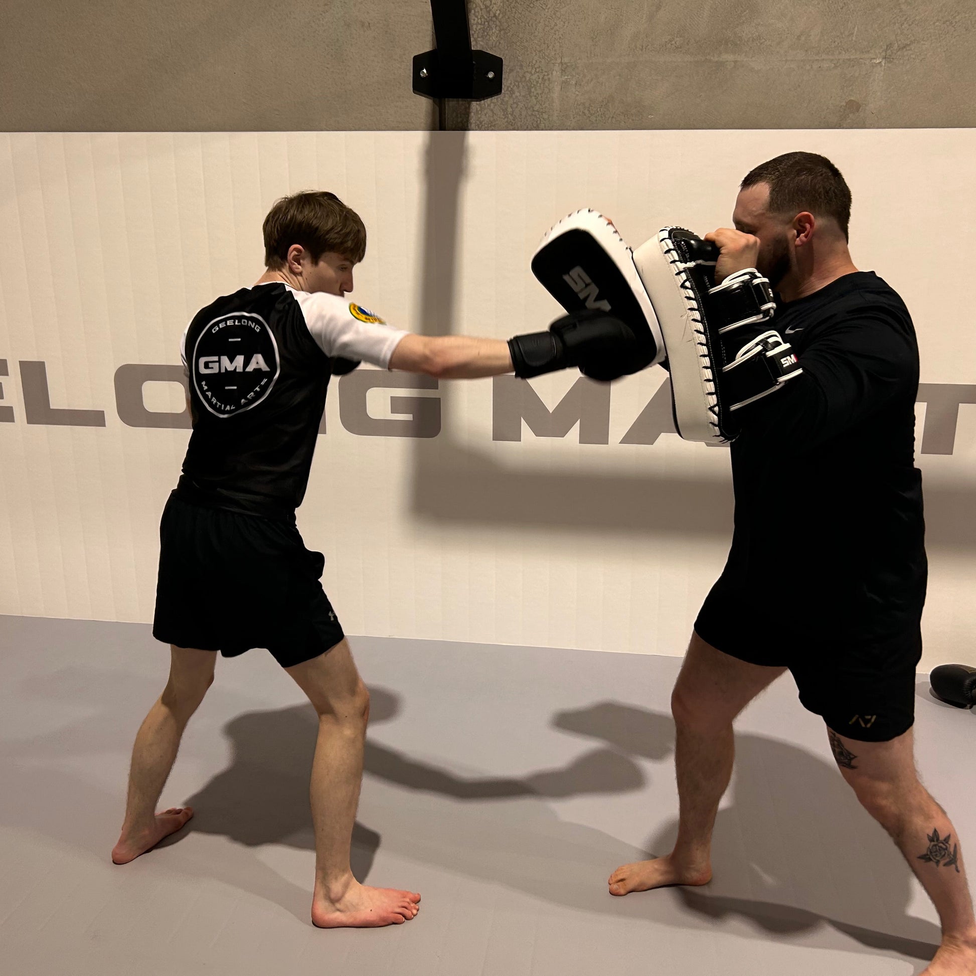 Two individuals practicing martial arts in a gym setting with 'GMA' branding.