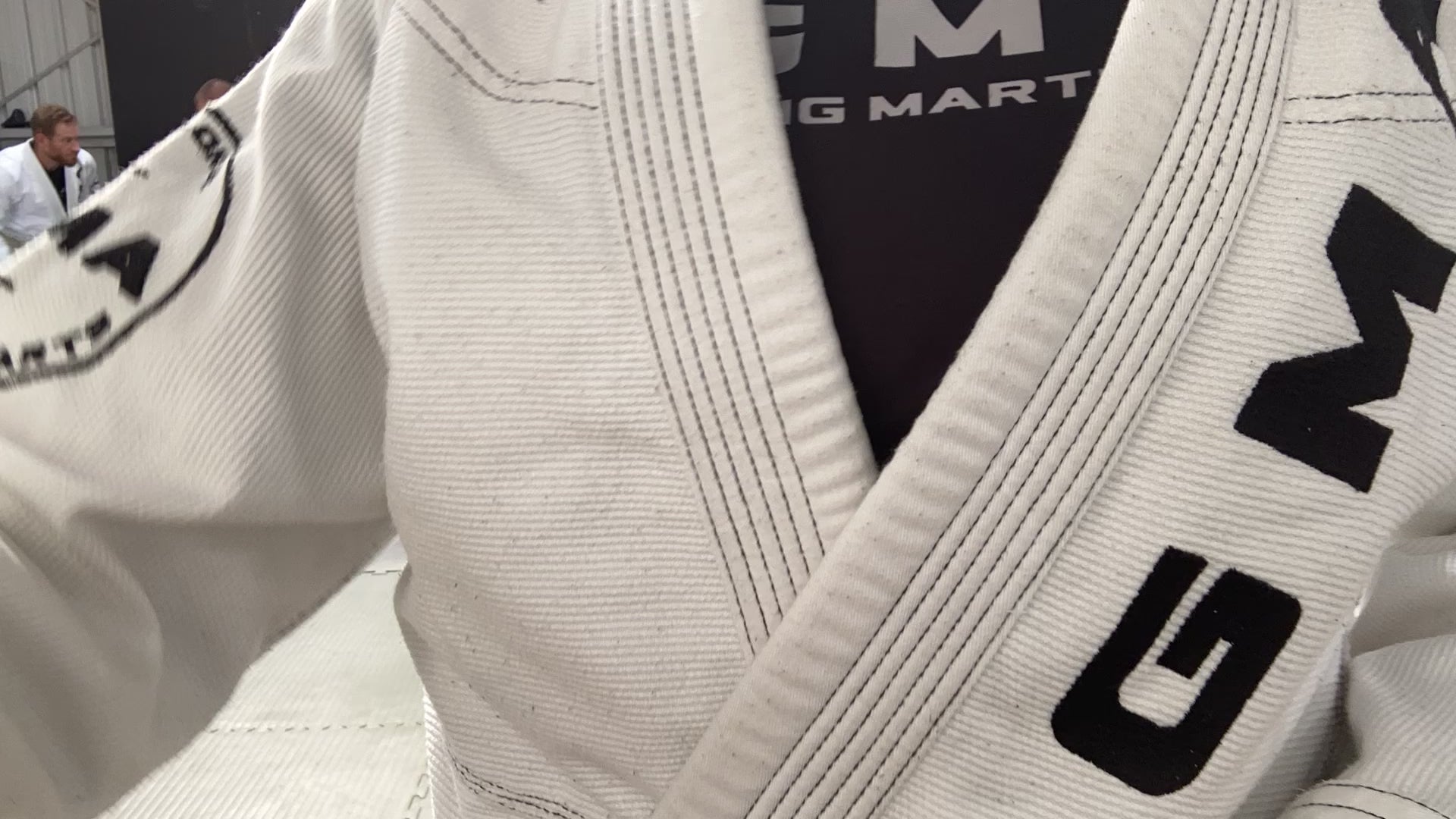 A speed up video of multiple pairs of adults wearing white BJJ gis branded with GMA wrestling on grey mats. 